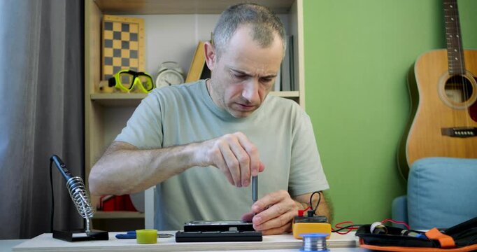 Man repairs electronic device with tools and precision. Focus on smartphone disassembly process. Workspace showcases organization and creativity. Ideal for technology and lifestyle content.