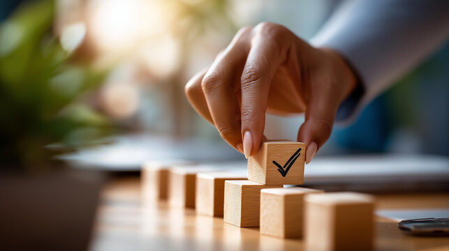 Close up of a hand placing a small wooden block with a checkmark icon onto a row of similar blocks on a clean bright surface milestone completion task done progress tracking