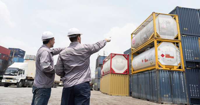 Chemical tanks or ISO tanks. Male workers in safety gear management loading chemical tanks at container yard. Industrial worker at work overseeing shipping ISO tanks and container at logistics yard