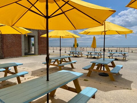 Blue picnic tables and yellow patio umbrellas in front of the concession stands in Jacob Riis Park in the Rockaways in Queens, New York City