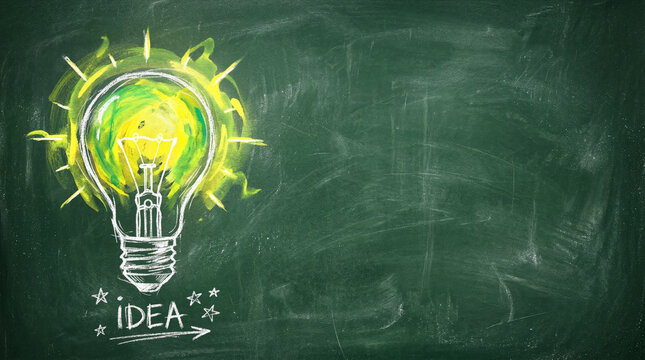 Creative idea concept with glowing yellow lightbulb drawn in chalk on green blackboard with copy space