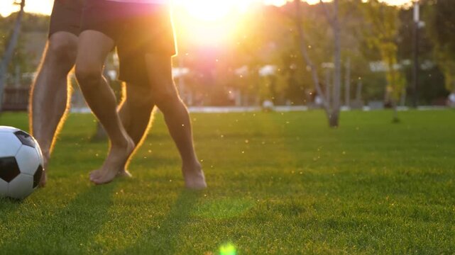 Father and son playing soccer together in park at sunset, running barefoot on green grass. Concept of active parenting, family bonding and healthy childhood, warm golden hour outdoor lifestyle.