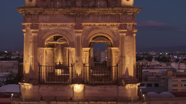 Cathedral Basilica of Immaculate Conception in Durango Mexico illuminated at dusk. Aerial drone footage captures ornate bell towers with baroque architecture and arched openings against city skyline.