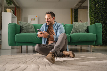 Fototapeta premium Man relaxing on floor using smart phone at home