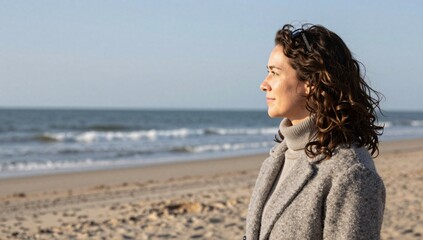 Obraz premium Woman gazes at the ocean horizon on a tranquil beach in a grey coat