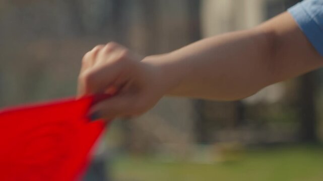 Caucasian Hand Waving Red Board Outdoors, Makeshift Fan Used To Control Smoke From Burn, Sunlit Backyard Setting, Wrist Motion And Grip Emphasized, Casual Gardener Action During Cleanup.