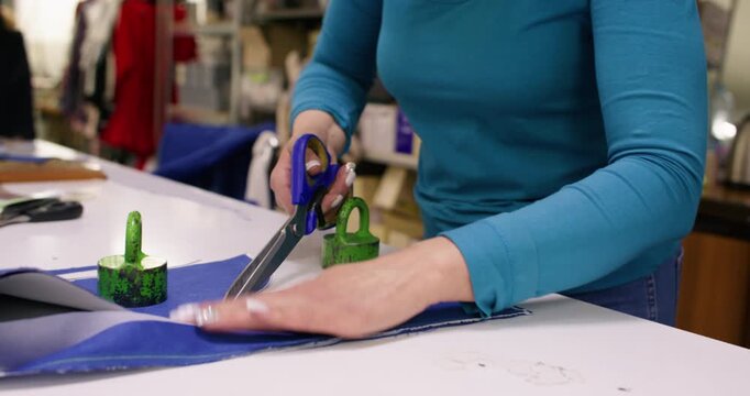 Dressmaking process. Designer fabric. Woman working with scissors on tailoring table. Seamstress creating clothes with curve paper draft.