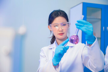 Fototapeta premium Asian woman chemist holding glassware testing liquid sample medical research and looking at purple chemical reaction laboratory glassware. Working clinical trial chemical analysis workspace.