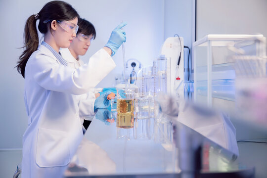 Asian female scientist using pipette to transfer liquid in biotechnology laboratory. Young chemist analyzing liquid chemical reaction in beaker for pharmaceutical industry