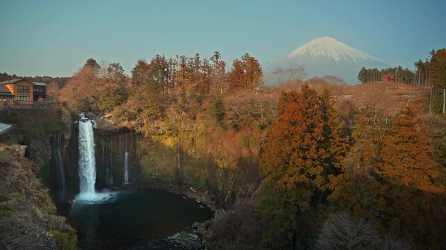 Scenic autumn landscape of Shiraito Falls with the snow-capped Mount Fuji in the background under a clear blue sky in Japan. A majestic and tranquil view capturing the natural beauty of Shizuoka