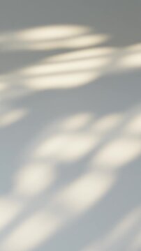 Sunlight casting a blurred window shadow moving on a neutral white wall creating a seamless loop background. Vertical video