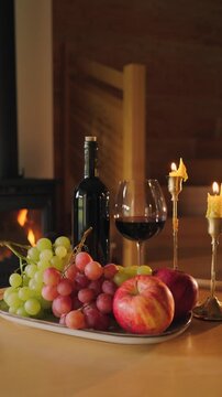 Slow living scene with wine, fruits and candles by fireplace. Cozy interior