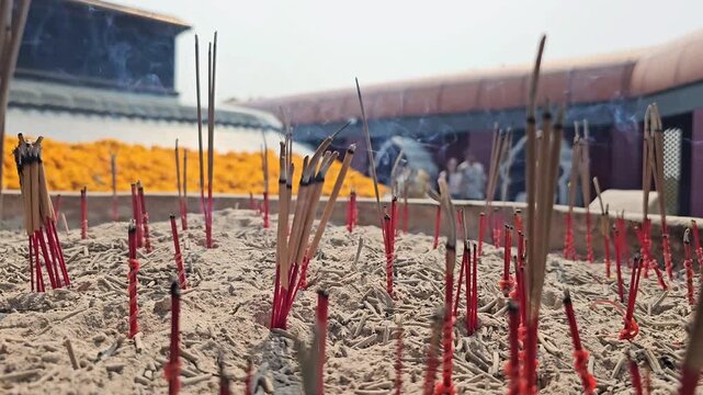 Burning incense sticks in ash with human hand placing joss sticks at outdoor temple altar. Close up footage of prayer ritual with rising smoke and spiritual offering in Asian religious culture