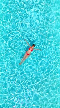 Top down view of a woman in pink swimsuit swimming on her back in the pool.