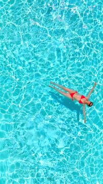 Top down view of a woman in pink swimsuit swimming on her back in the pool.