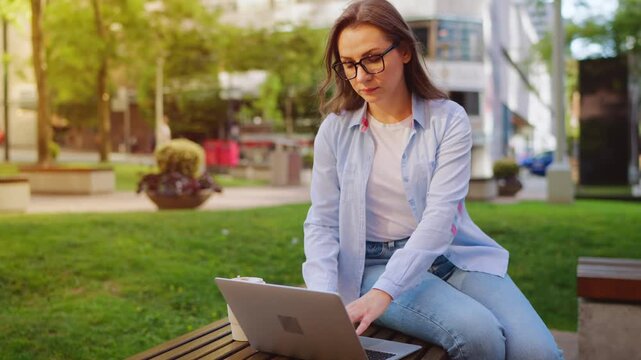 A woman sitting in the park with a laptop and working during the summer day