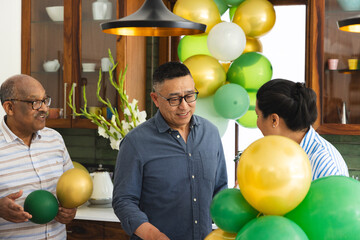 Fototapeta premium Diverse family with senior men and woman decorating with green and gold balloons in kitchen
