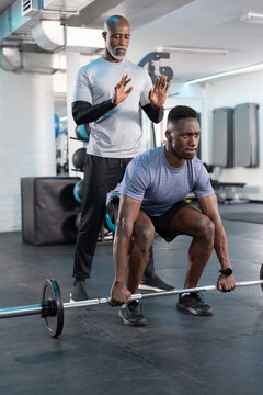 Male lifter responding to coach cue, performing loaded barbell squat in gym for strength training