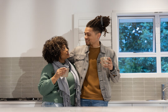 Couple making eye contact while holding ceramic mugs at kitchen countertop near gas cooktop