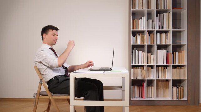 Man in shirt and tie juggling a small soccer ball at his home office desk, ignoring his laptop and papers, illustrating procrastination, distraction and lack of focus