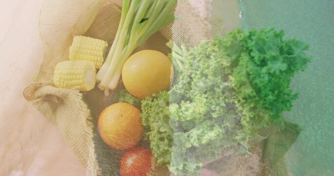 Showing top view produce cluster sitting on burlap tabletop, with corn scallions citrus tomato kale