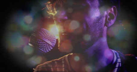 Fototapeta premium Male singer in striped shirt singing into handheld mic at concert, with backlight haze bokeh