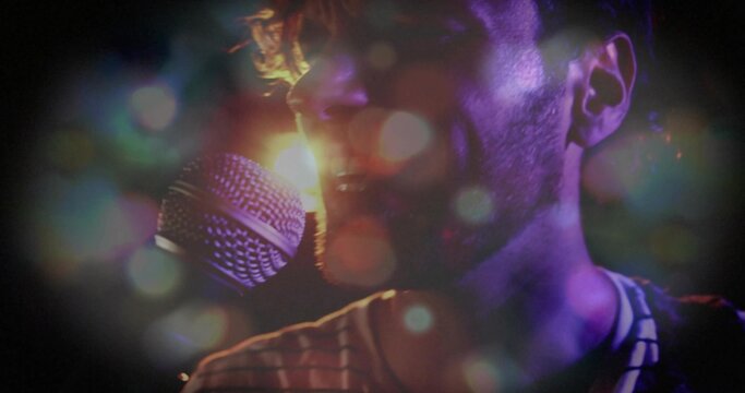 Male singer in striped shirt singing into handheld mic at concert, with backlight haze bokeh