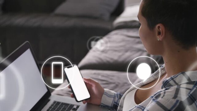Woman holding phone plus laptop on couch, phone lighting, icons appearing, syncing, fading, tech