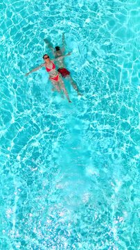 Top down view as a man dives into the pool while woman is laying on her back