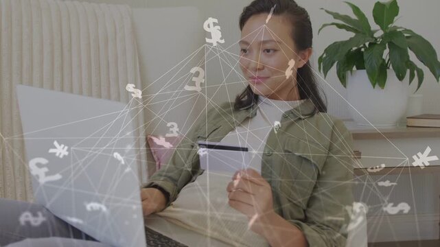 Woman holding credit card and typing on laptop causing animated currency overlay for online payment