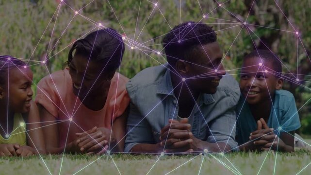 Family lying on grass, talking, man turning toward boy as tech network drifting, linking nodes