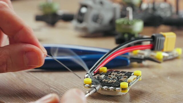 Technician soldering components onto circuit board of disassembled fpv drone