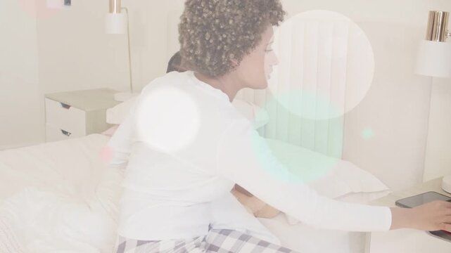 Woman checking child's temp on bed with teddy, then tapping phone showing health color circles