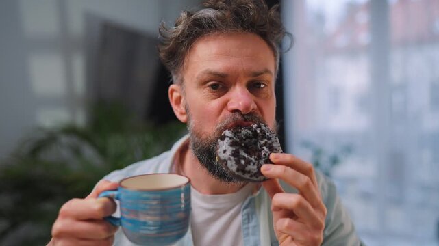 Sweet addiction concept. A man eats a donut and drinks coffee.