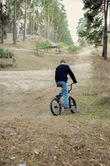 Naklejka premium Teenager Riding BMX Bicycle on Sandy Trail in Pine Forest Outdoor Adventure and Active Lifestyle