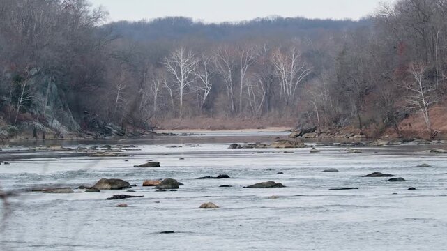 View of the Potomac River flowing through rocky terrain and bare trees at Scott's Run Nature Preserve in McLean, Virginia, United States.