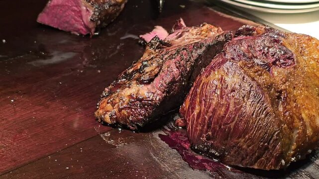 Sliced roasted beef brisket and smoked meat cuts on wooden carving board with meat juices and crispy crust in restaurant kitchen buffet serving close up. Barbecue and steakhouse food preparation conce