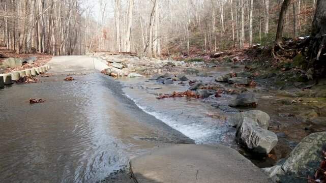 View of a stream flowing over a concrete crossing at Scott's Run Nature Preserve with bare trees and rocks in McLean, Virginia, United States.