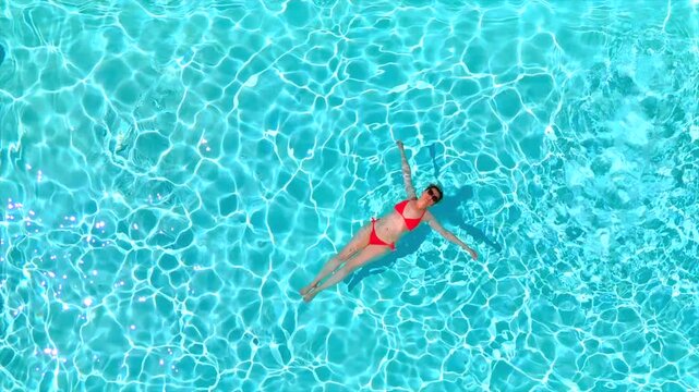 Top down view of a woman in pink swimsuit swimming on her back in the pool.