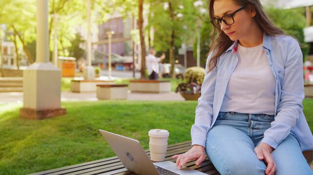 A woman sitting in the park with a laptop and working during the summer day