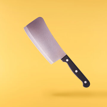 Levitating heavy metal meat cleaver butcher knife with black handle isolated on a solid yellow background. Minimalist zero gravity concept.
