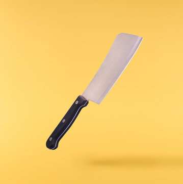 Levitating heavy metal meat cleaver butcher knife with black handle isolated on a solid yellow background. Minimalist zero gravity concept.