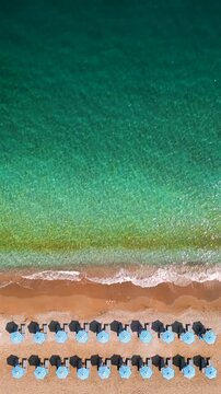 Top-down view of sandy beach with sun umbrellas and turquoise sea water