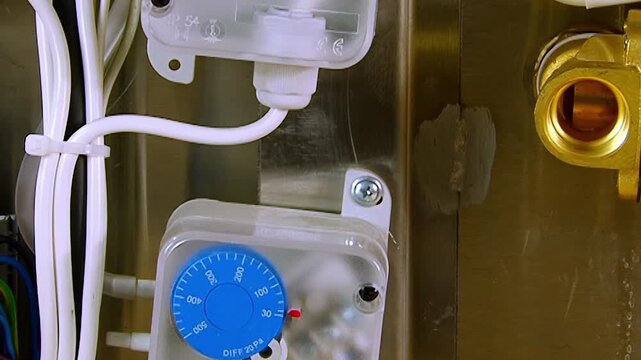 A close up reveals multiple differential pressure switches, connected by neat white wiring on a shiny metallic panel.
