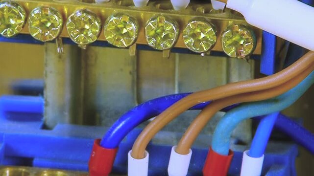 Vibrant electrical conductors merge at shining terminal block. Technician's tool meticulously checks each connection point, orchestrating complex power distribution in modern workshop during day.