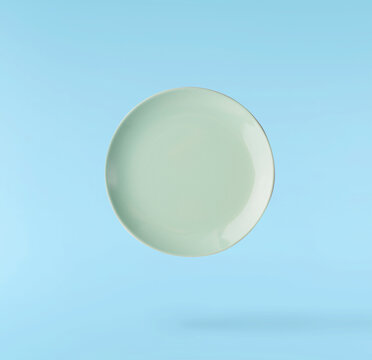 Levitating empty ceramic plate isolated on a pastel blue background. Minimalist zero gravity studio tableware photography concept.
