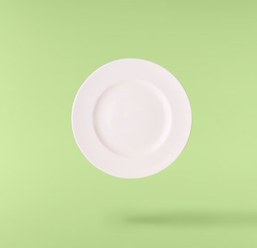 Levitating empty ceramic plate isolated on a green background. Minimalist zero gravity studio tableware photography concept.