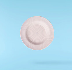 Obraz premium Levitating empty ceramic plate isolated on a pastel blue background. Minimalist zero gravity studio tableware photography concept.