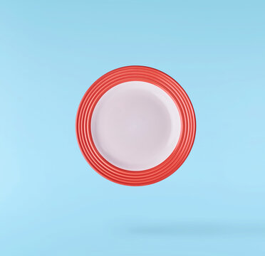 Levitating empty ceramic plate isolated on a pastel blue background. Minimalist zero gravity studio tableware photography concept.