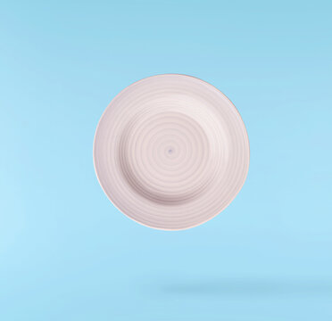 Levitating empty ceramic plate isolated on a pastel blue background. Minimalist zero gravity studio tableware photography concept.